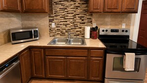 A kitchen with wooden cabinets, a stainless steel microwave, a double sink, a stove, and a tiled backsplash.