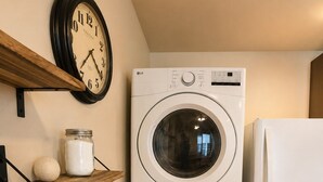 A laundry area with a stacked washer and dryer, a clock, and a shelf with a jar and a ball. - Farm Charm in Downtown Cheyenne (Cheyenne)