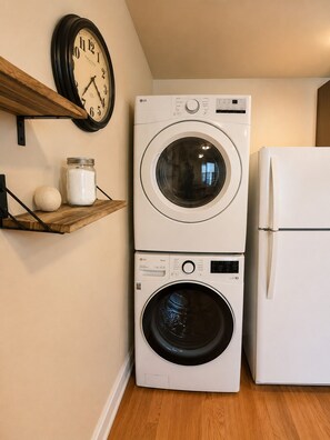 A laundry area with a stacked washer and dryer, a clock, and a shelf with a jar and a ball. - Farm Charm in Downtown Cheyenne (Cheyenne)