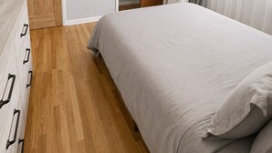 A bedroom with a bed, wooden floor, ceiling fan, closet, and window with curtains.