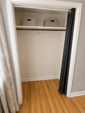 A closet with two storage boxes, a hanging rod, and a partially drawn curtain. - Spacious Duplex that is pet friendly (Cheyenne)