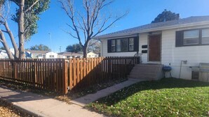 A single-story house with a front yard, a wooden fence, and a clear sky.