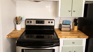 Une cuisine équipée d’une cuisinière en acier inoxydable, d’un four noir et de meubles de couleur vert clair.