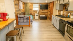 Quarto compacto com cama, cozinha compacta e televisão fixada na parede.