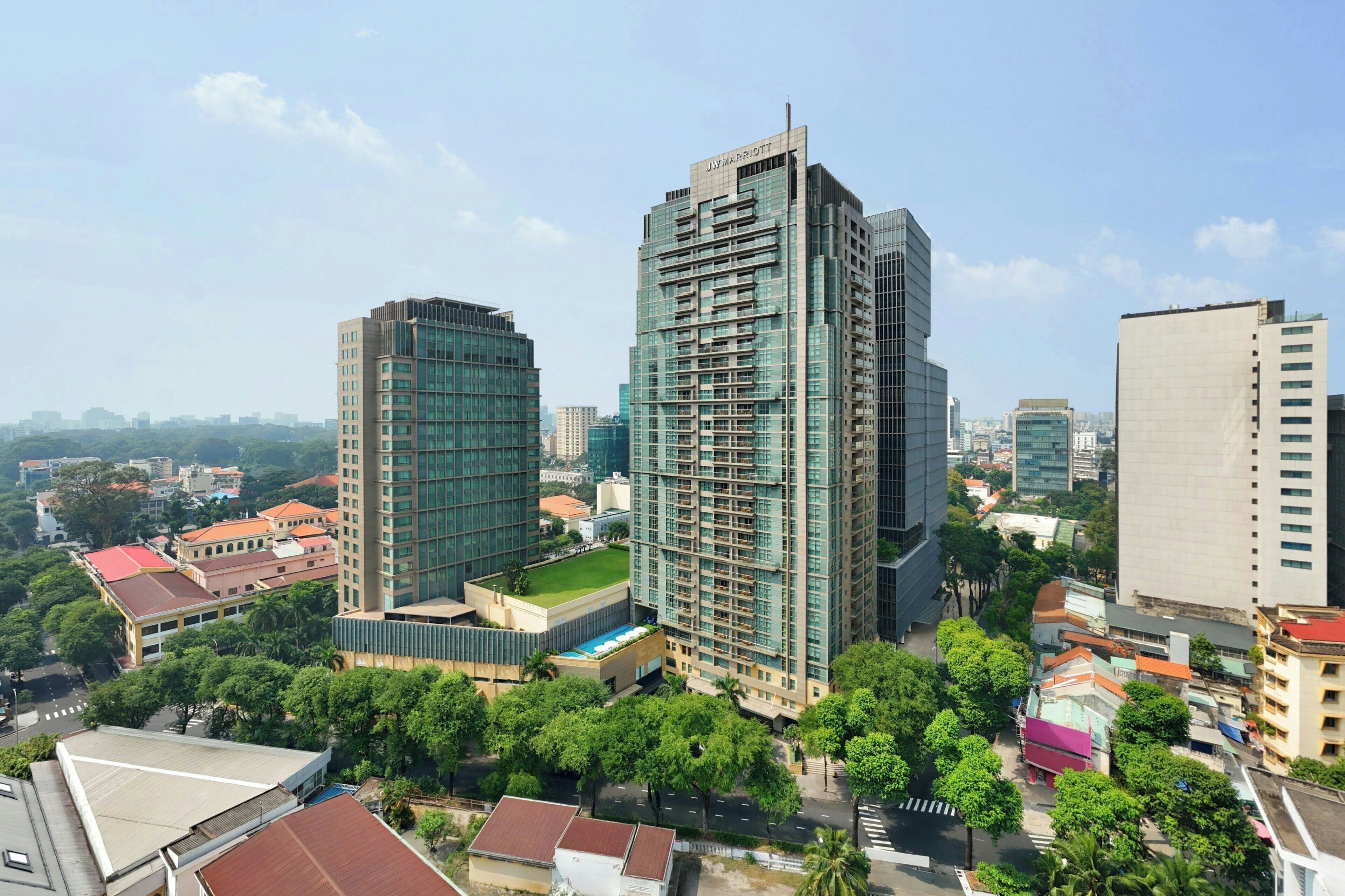 Un hotel moderno de gran altura con fachada de vidrio, rodeado de otros edificios y zonas verdes.