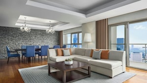 A modern living room with a sectional sofa, dining table, and chairs, a chandelier, and large windows offering a city view.