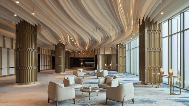 A spacious lobby with modern furniture, large windows, and a unique ceiling design.