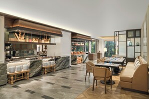 Eine moderne Hotelhalle mit einer Marmor-Rezeption, einem Essbereich mit Tischen und Stühlen sowie einer Sitzecke mit einer Couch.