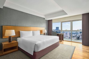 Ein modernes Hotelzimmer mit einem großen Bett, zwei Nachttischen, einem Schreibtisch und Blick auf die Stadt.