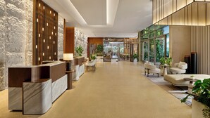 A modern lobby with a reception desk, seating area, and large windows.