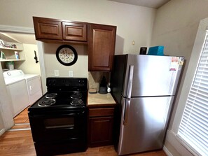 A compact kitchen with a black stove, stainless steel refrigerator, wooden cabinets, and a wall clock. - Duplex close to downtown Cheyenne (Cheyenne)