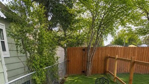 Un jardin avec une zone délimitée par une clôture, une clôture en bois, une table en métal avec des chaises et une terrasse en béton.