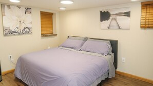 A bedroom with a bed, a window with blinds, and two wall-mounted artworks. - Cozy Cottage Basement Apartment (Cheyenne)