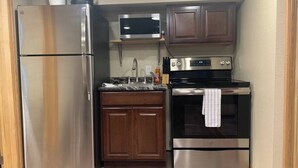 Une cuisine de taille réduite, dotée d’un réfrigérateur en acier inoxydable, d’un four à micro-ondes, d’une cuisinière et d’armoires en bois.