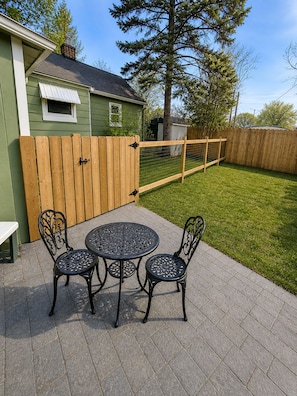 A patio with a round table and chairs, a wooden fence, and a green building in the background. - Cozy cottage in Cheyenne (Cheyenne)