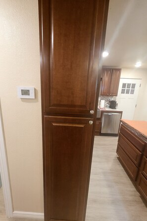 A kitchen with wooden cabinets, a stainless steel refrigerator, and a digital thermostat on the wall. - Cozy cottage in Cheyenne (Cheyenne)