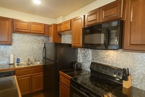 Une cuisine avec des meubles de rangement en bois, un réfrigérateur noir, un four à micro-ondes, une cuisinière et un évier.