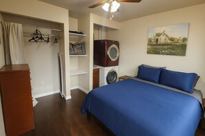 Un dormitorio con cama, armario, lavadora y secadora integradas, y un cuadro en la pared.