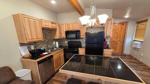 A modern kitchen with wooden cabinets, a black refrigerator, a microwave, and a glass-top island with stools. - Cheyenne Frontier Apartment (Cheyenne)