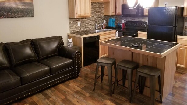 A modern kitchen with wooden cabinets, a black refrigerator, and a central island with stools. - Cheyenne Frontier Apartment (Cheyenne)
