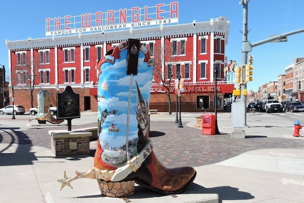 Une grande sculpture colorée représentant un chapeau de cowboy et des bottes, placée devant un bâtiment sur lequel est affiché un panneau indiquant : « The Wrangler, célèbre pour ses vêtements de travail depuis 1943 ».