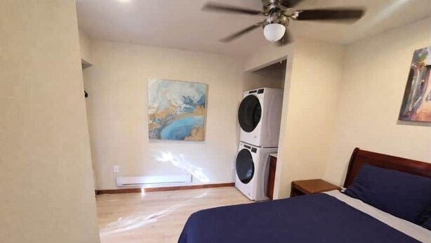 Un dormitorio con cama, ventilador de techo, lavadora y un cuadro en la pared.