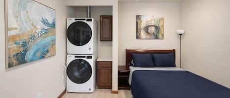 A bedroom with a bed, a ceiling fan, a washing machine, and a painting on the wall.