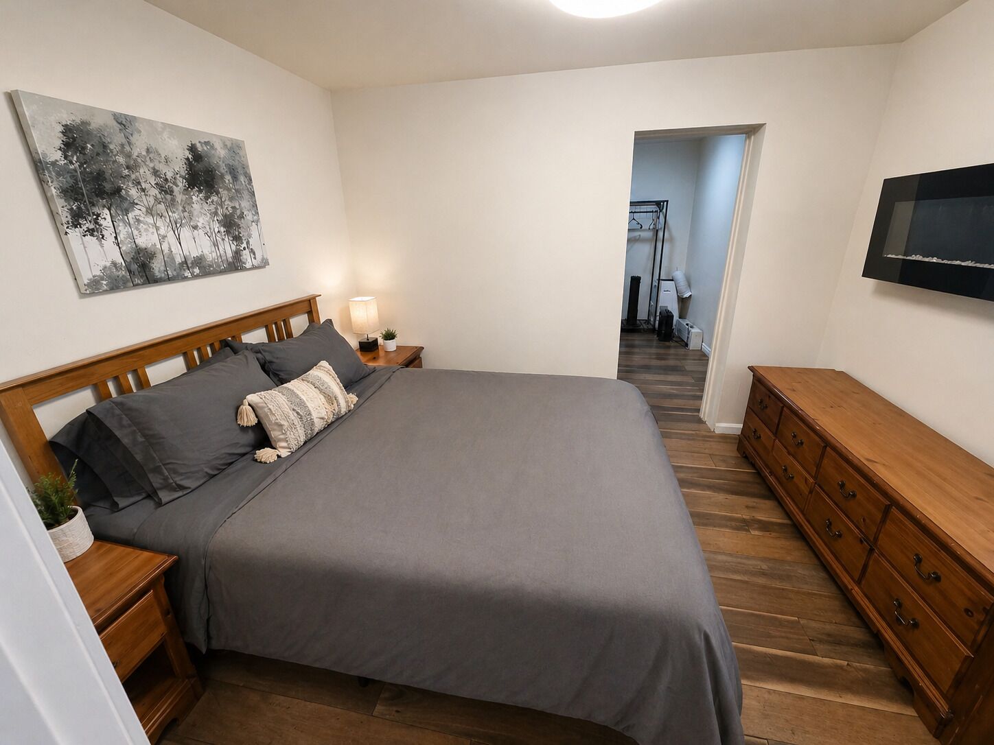 Une chambre à coucher comprenant un lit, des tables de chevet, une commode, un téléviseur et un couloir menant à une salle de bain.
