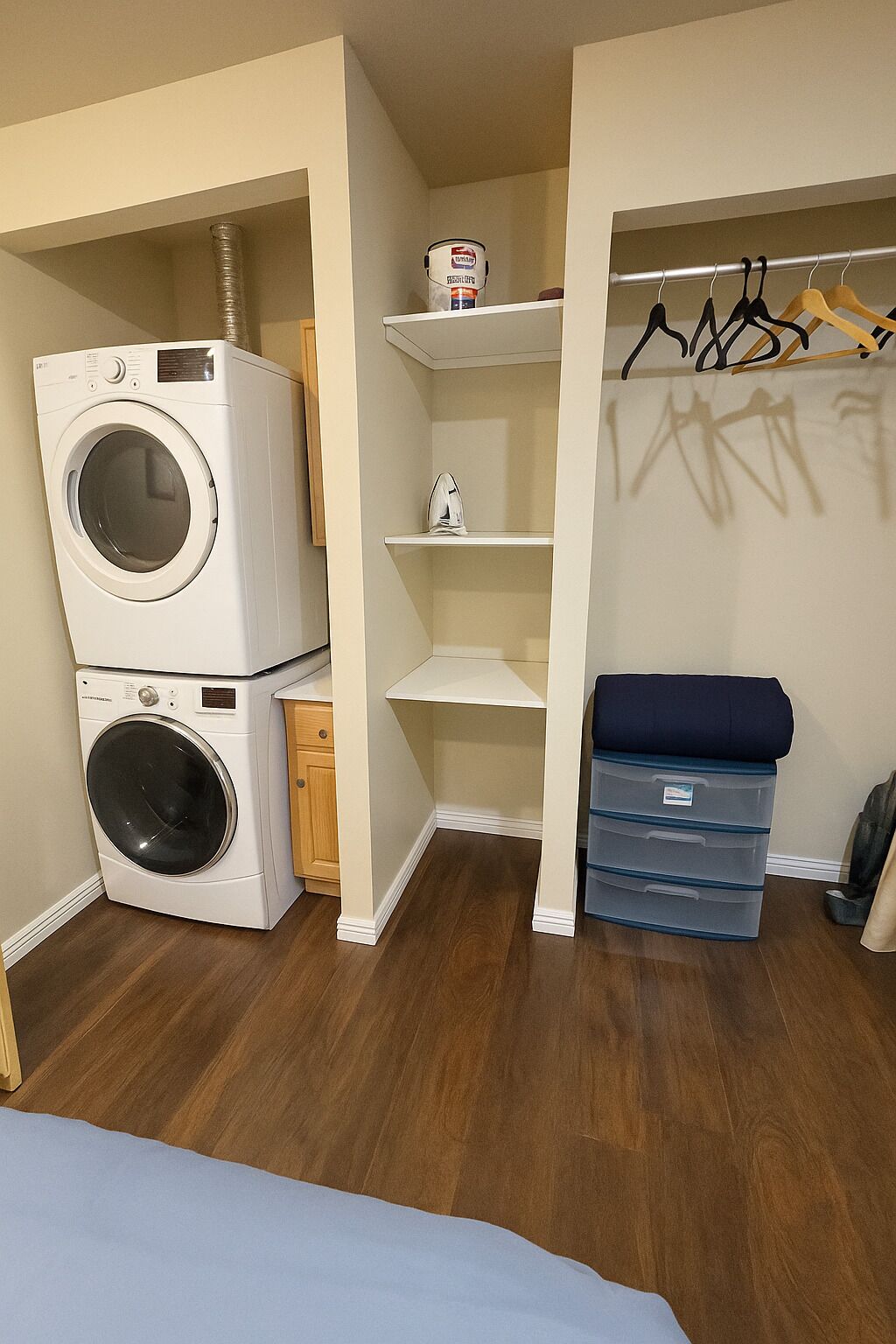 Une petite buanderie comprenant une machine à laver et un sèche-linge superposés, une étagère avec un bidon de lessive et un portant à vêtements avec des cintres.