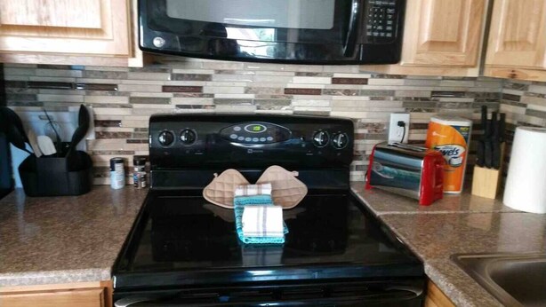 A kitchen with a black stove, a microwave above it, and wooden cabinets. - Cheyenne Frontier Homes #4 (Cheyenne)