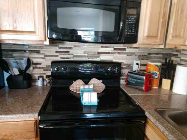 A kitchen with a black stove, a microwave above it, and wooden cabinets.