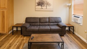 A living room with a brown leather sofa, a wooden coffee table, and a painting of two trees on the wall. - Cheyenne Frontier Homes #4 (Cheyenne)