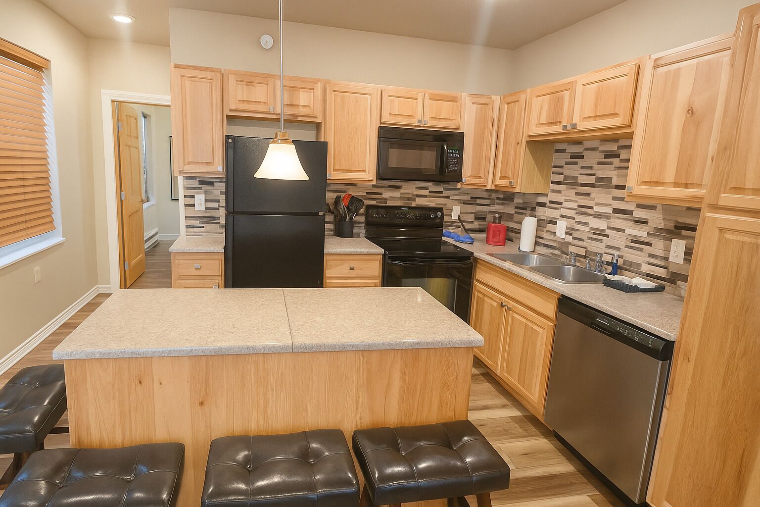 A modern kitchen with wooden cabinets, a black refrigerator, a microwave, a stove, and a dishwasher. There is a granite countertop and a hanging light fixture.
