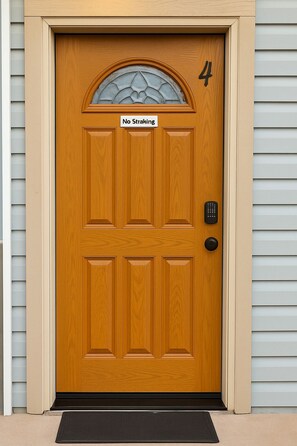 Une porte d’entrée en bois avec une pancarte indiquant « Interdiction de coller des autocollants », un clavier pour ouvrir la porte et le chiffre « 4 » au-dessus.