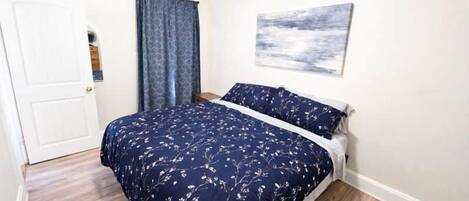Une chambre à coucher avec un lit, une porte, une fenêtre avec des rideaux et un tableau accroché au mur.
