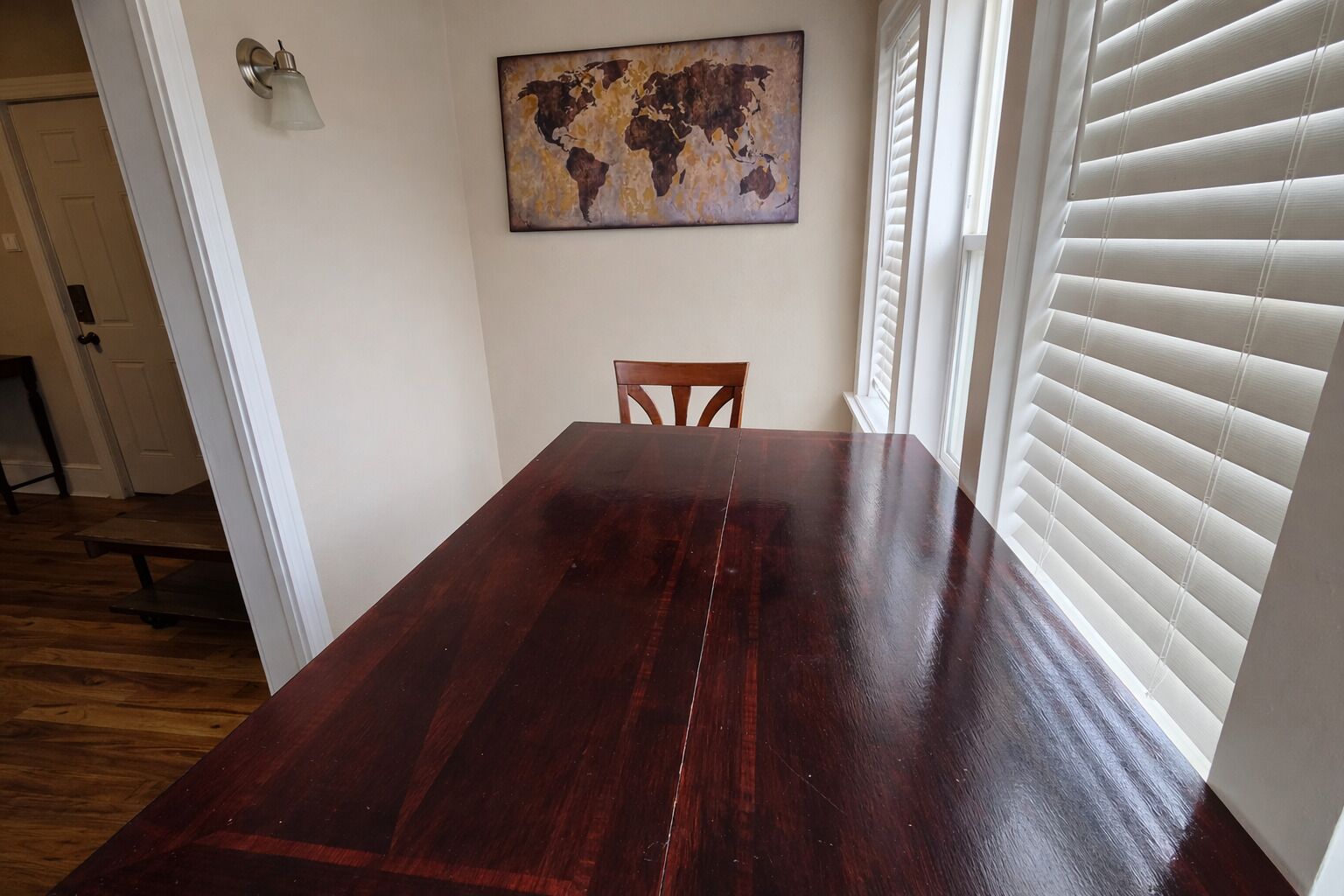 Una sala da pranzo con un tavolo e sedie in legno, un quadro raffigurante una mappa del mondo e una finestra con persiane.