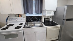 Una cocina compacta con armarios blancos, estufa, pileta, microondas y heladera.