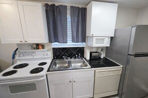 A compact kitchen with white cabinets, a stove, a sink, a microwave, and a refrigerator.
