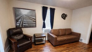 A living room with a brown leather sofa, a brown leather armchair, a small wooden table, and a framed picture on the wall. - Downtown Cheyenne Home West Wing (Cheyenne)