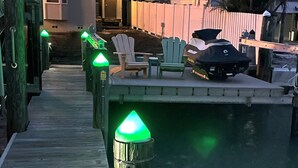 Eine Holzsteg mit grünen Lichtern, einem Jetski und einer Reihe von Stühlen am Wasser.