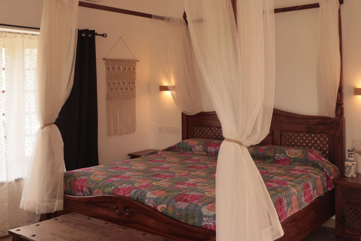 A four-poster bed with a canopy, a wooden chest, and a macramé wall hanging.