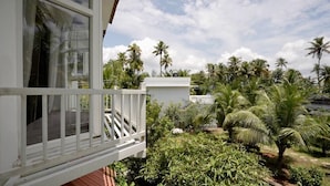 Een balkon met een witte reling, uitkijkend op een tuin met palmbomen en ander groen.