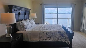 A bedroom with a large bed, two bedside lamps, a view of a body of water through a large window, and a dark headboard. - Waterfront 5BR/5.5BA Home w/ 2 Docks and Private pool and spa (Montgomery)