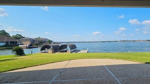A waterfront view with a covered outdoor seating area, a grassy lawn, and a clear sky. - Waterfront 5BR/5.5BA Home w/ 2 Docks and Private pool and spa (Montgomery)