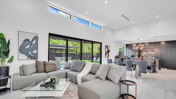 A modern living room with a sectional sofa, a glass coffee table, and a dining area with a kitchen in the background.