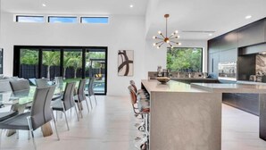 A modern kitchen with a central island, large windows, and a dining area with glass tables and chairs.