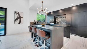 A modern kitchen with a central island, bar stools, and a large window.