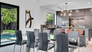 A modern kitchen with a dining area, large windows, and a view of a swimming pool.