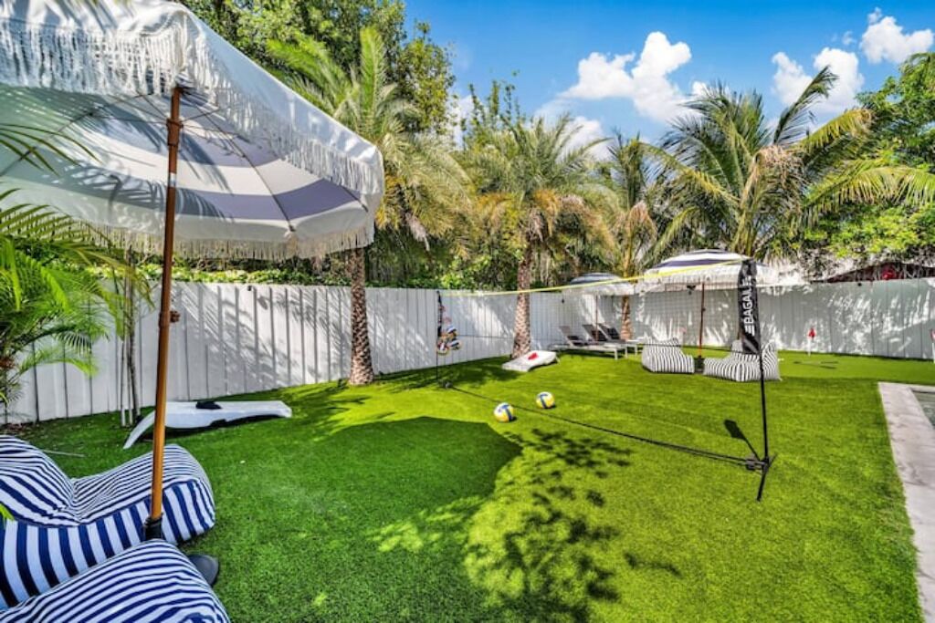 A backyard with artificial grass, a hammock, a tiki bar, and palm trees.
