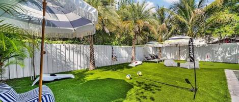 A backyard with artificial grass, a hammock, a tiki bar, and palm trees.